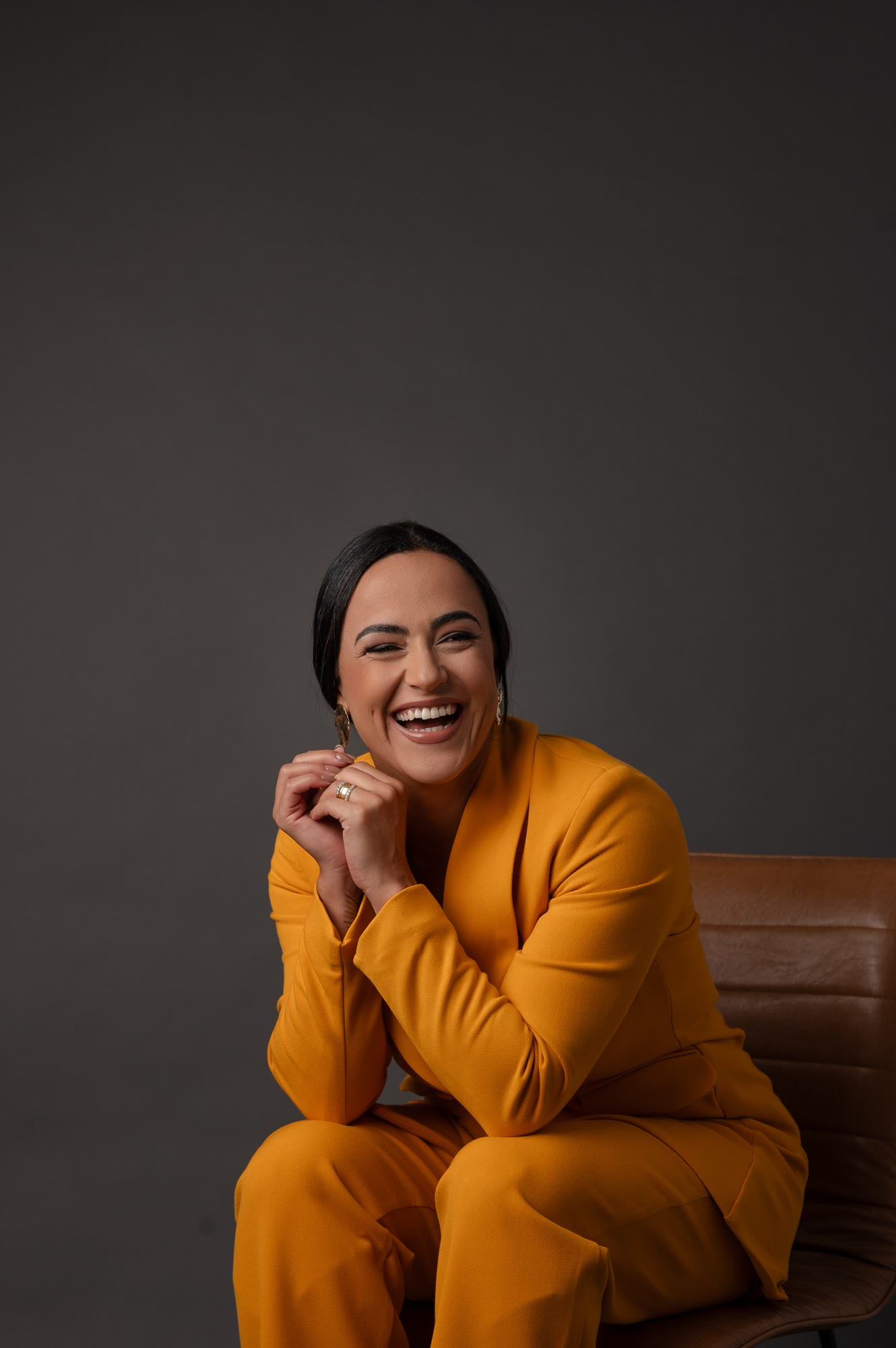 Camila Meneses rindo, sentada, de terno mostarda